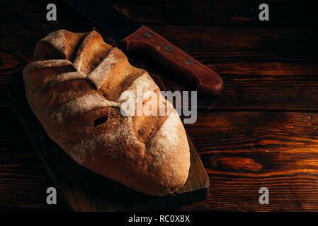 Hausgemachtes Brot auf Schneidebrett mit Messer auf dunklem Hintergrund. Stockfoto