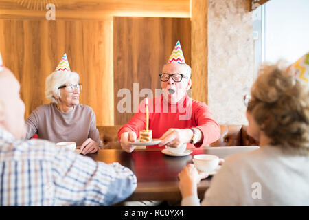 Älterer Mann ausblasen Kuchen Kerze aufgeregt Stockfoto