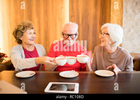 Freundliche ältere Freunde klirren Kaffeetassen Stockfoto