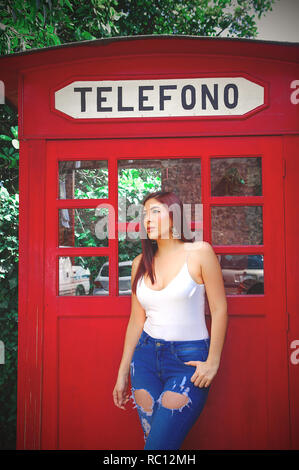 Quito, Ecuador, 12. Dezember 2018: Im freien Blick auf die schöne junge Frau trägt ein weißes Hemd und Jeans vor der Roten Telefonzelle in der Stadt Quito posiert im Norden Ecuadors Stockfoto