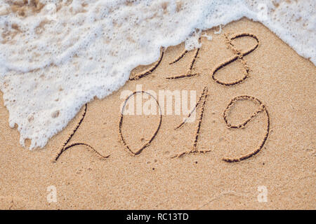 Neues Jahr 2019 kommt Konzept - Inschrift 2018 und 2019 auf einem Strand Sand, die Welle ist fast für die Ziffern 2018 Stockfoto