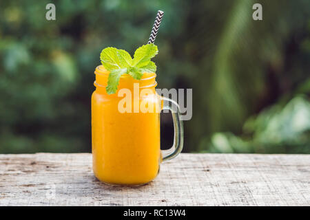 Mango Smoothie in einem Glas Marmeladenglas und Mango auf grünem Hintergrund. Mango schütteln. Tropische Früchte Konzept Stockfoto