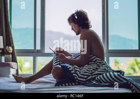 Der Mann wachte am Morgen und Lesen von Nachrichten auf dem Tablett im Hintergrund ein Fenster mit Blick auf die Berge Stockfoto