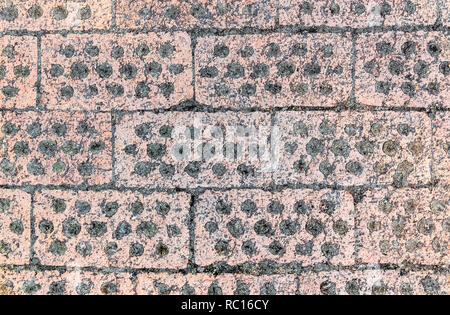 Hintergrund von Pflastersteinen mit Bohrungen für das Wachstum des Grases in einem buddhistischen Tempel. Stockfoto