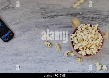 TV-Fernbedienung und Schüssel mit Popcorn auf weißem Hintergrund. Fernsehen Konzept/Bereit für Spaß-Image Stockfoto