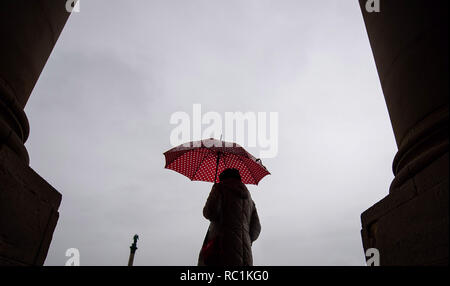 Stuttgart, Deutschland. 13 Jan, 2019. Eine Frau mit ihrem roten Regenschirm steht zwischen zwei Spalten. Credit: Sebastian Gollnow/dpa/Alamy Leben Nachrichten Quelle: dpa Picture alliance/Alamy leben Nachrichten Stockfoto