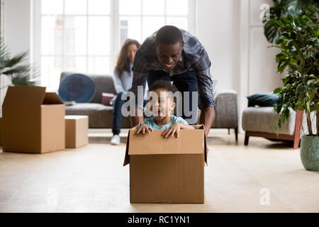 Afrikanische Sohn Lachen von Reiten in Box mit Vati aufgeregt Stockfoto