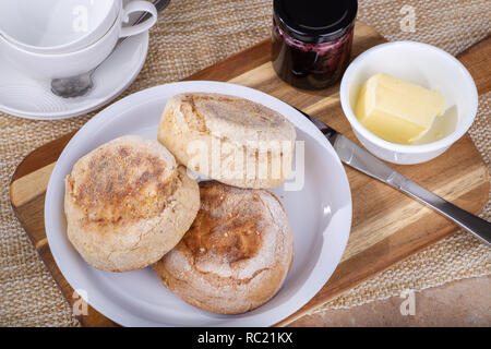 Ansicht von oben auf einen Teller zu Englische Muffins die mit Butter und Marmeladenglas auf einem Holzbrett Stockfoto