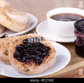 Englische Muffins mit Blaubeer-marmelade verteilt auf einem Teller mit Tasse Kaffee im Hintergrund Stockfoto