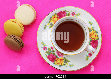 Schwarzer Tee in vintage Porzellan Tasse mit makronen auf lebhaften Rosa Oberfläche Stockfoto