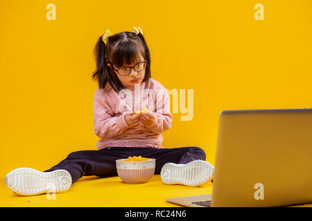 Interessierte kleine Dame mit Down Syndrom essen Chips Stockfoto