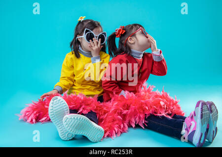Zwei glückliche Mädchen sitzen auf Studio beim Tragen der Brille Stockfoto