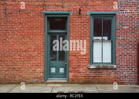 Ein altes Holz Rahmen von Tür und Fenster grün lackiert gegen eine verwitterte Red brick wall in der kleinen Stadt Elizabeth City, North Carolina. Stockfoto