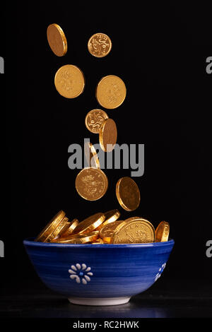 Pot of Gold Konzept mit Schokolade Gold Münzen fallen in einen Topf auf einem schwarzen Hintergrund Stockfoto