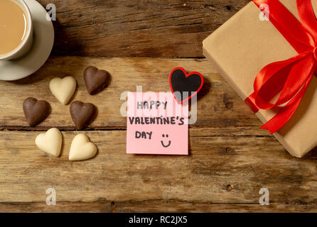 Schöne Ansicht von oben Valentines Zusammensetzung von Geschenk, Schokolade in Herzform, Kaffee und Happy Valentines Tag Hinweis auf Post-it im Vintage Stil geschrieben wird Stockfoto