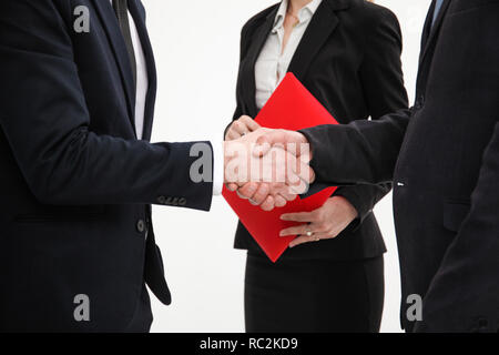 Nahaufnahme von einem festen Händedruck zwischen zwei Kollegen nach der Unterzeichnung eines Vertrags, der Sekretärin im roten Ordner halten Stockfoto