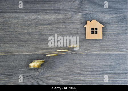 Das Symbol einer Bambus Haus auf einer hölzernen rustikalen grauer Hintergrund mit Leuchtendgelben Münzen in der Form von Schritten das Ziel kaufen ein Haus zu erreichen. Stockfoto