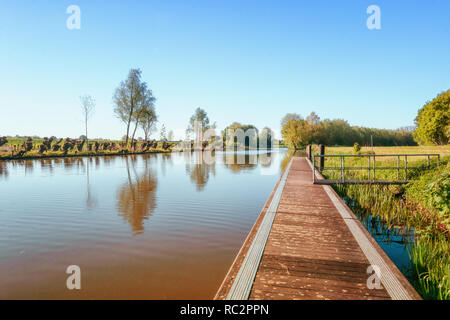 Einen langen Steg entlang des Flusses Linge in der Betuwe Region in den Niederlanden mit einer Reihe von Weiden auf der anderen Seite Stockfoto