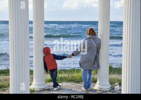 Erwachsene Frau die Hand des kleinen Zicklein in der Jacke zu Spalten in der Nähe von Sturm Meer im Freien Stockfoto