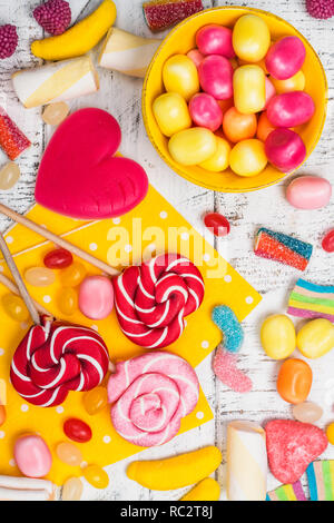 Rosa Bonbons, Lutscher und Jelly Beans auf weißem Holz- Hintergrund. Süße Grußkarte. Kopieren Sie Platz. Ansicht von oben Stockfoto