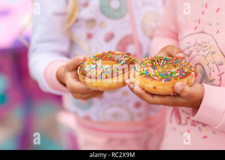 Zwei Mädchen halten einen süßen und einen großen Donut mit rosa Zuckerguss und Süßwaren dressing eingerichtet Stockfoto