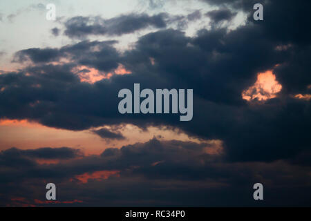 Sonnenuntergang mit dunklen Wolken, in Orange und lila Farbtönen Stockfoto