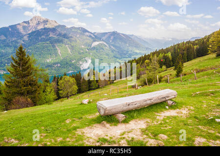 Log Bank am Hang eines Berges Zwoelferhorn in den österreichischen Alpen. Schöne Aussicht auf den Wolfgangsee See und Schafberg an einem sonnigen Frühlingstag. Stockfoto