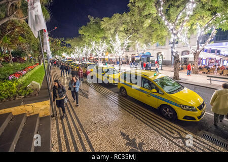 Menschen zu Fuß entlang der von Bäumen gesäumten Allee Avenida 'Ehe' in Funchal, Madeira in der Nacht. Stockfoto