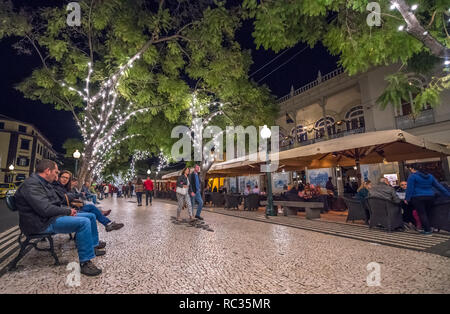 Menschen zu Fuß entlang der von Bäumen gesäumten Allee Avenida 'Ehe' in Funchal, Madeira in der Nacht. Stockfoto