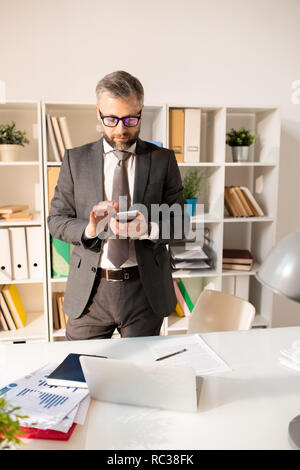Bärtige Geschäftsmann in Anzug mit Smartphone im Büro Stockfoto
