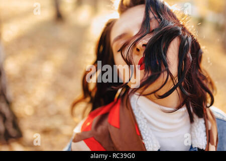 Junge hübsche Mädchen mit roten Lippen und kurze Haare in einem Denim coat Wanderungen im Herbst sonnige Stadt Stockfoto