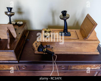 Antike hölzerne Bilderrahmen an der vorderen Wand Telefone, Dom nach oben zurück, hängende pony Empfänger, & schräg schreiben Plattform, flach auf Holztisch. Stockfoto