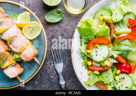 Gegrillte Spieße von Lachs und gesunde Gemüse Salat von frischen Tomaten, Gurken, Salat und Getreide auf Platte, Ansicht von oben. Diätmenü. Stockfoto