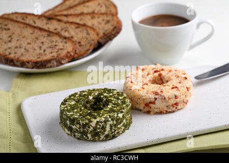 Umläufe des Lettischen Käse mit grünen, Muttern und Pfeffer auf einem keramischen Schneidebrett für Frühstück mit Kaffee Stockfoto