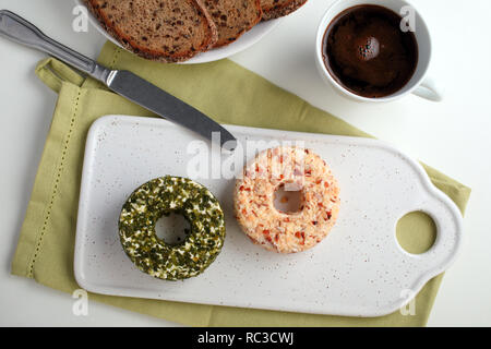 Umläufe des Lettischen Käse mit grünen, Muttern und Pfeffer auf einem keramischen Schneidebrett für Frühstück mit Kaffee Stockfoto