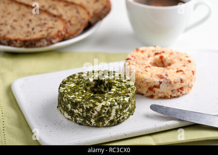 Umläufe des Lettischen Käse mit grünen, Muttern und Pfeffer auf einem keramischen Schneidebrett für Frühstück mit Kaffee Stockfoto