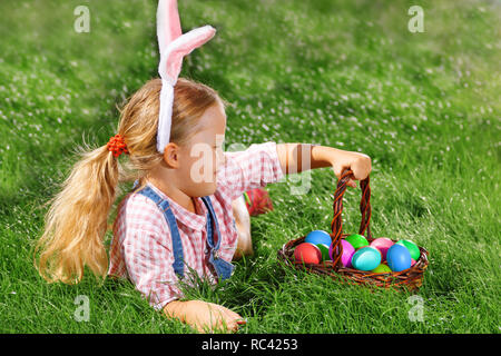 Süße kleine Mädchen mit Korb auf grünem Gras im Park. Easter Egg Hunting Konzept Stockfoto