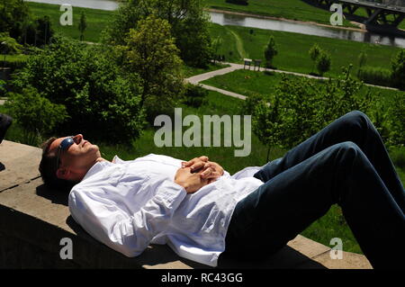 Mann mit weißem Hemd und Sonnenbrille liegt an der Wand, in Dresden und genießt den Blick über das Elbtal. Stockfoto