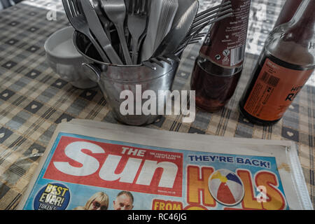 Nahaufnahme der Sonne Zeitung Impressum auf einen typisch englischen Transport Cafe Tabelle mit allen Besteck in einen Eimer und Würzmittel Stockfoto