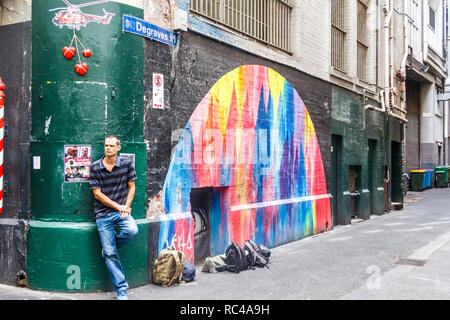 Melbourne, Australien - 21. Februar 2018: Ein Mann gegen eine Wand von einem Wandgemälde, lehnend. Die Gassen sind berühmt für Wand Kunst Stockfoto