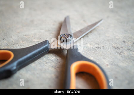 Schwarz und orange gefärbten Scheren auf einem grauen Tabelle gehalten Stockfoto