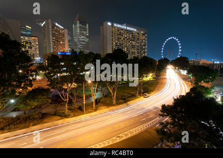 Der Verkehr in leichten Wanderwegen zum Singapore Flyer, ein gigantisches Riesenrad, in Singapur in der Abenddämmerung. Mehrere berühmte Hotels sind im Hintergrund. Stockfoto