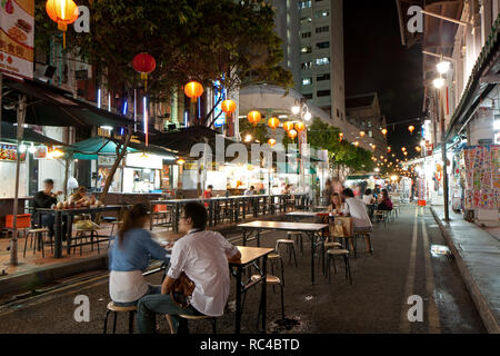 Mehrere Touristen sitzen und essen im Freien an der Straße auf Smith Street in Singapur Chinatown, nachts. Stockfoto