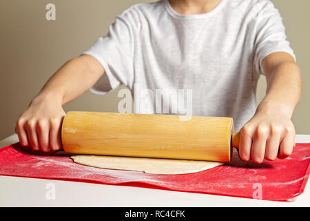 Kid Hände rollen Sie den Teig mit dem Nudelholz auf Silikon Teig rollen und Backen mat Stockfoto