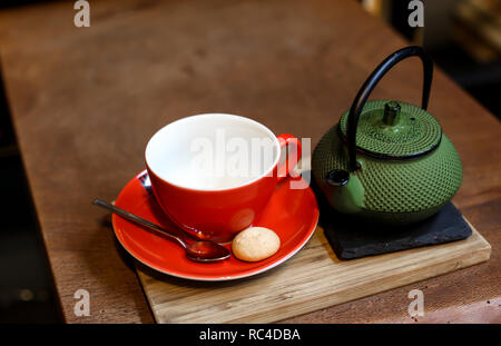 Chinesischer grüner Tee pot und rot Tasse Kräutertee auf dem rauen Holz- Tabelle. Erholsame Zeit von der Reise und der Aufnahme von Fotos im Coffee Shop. Stockfoto