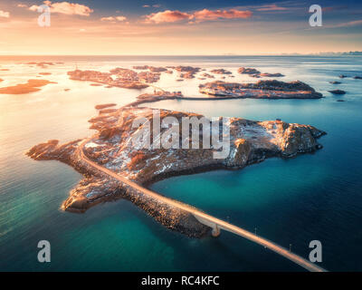 Luftaufnahme der Brücke über das Meer und die Berge auf den Lofoten Inseln, Norwegen. Henningsvær bei Sonnenuntergang im Winter. Landschaft mit azurblauem Wasser, Himmel mit go Stockfoto