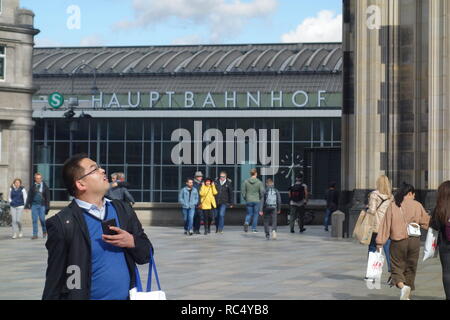 Eine asiatische Touristen mit einer Kamera blickt auf den Kölner Dom mit dem Kölner Hauptbahnhof im Hintergrund. Stockfoto