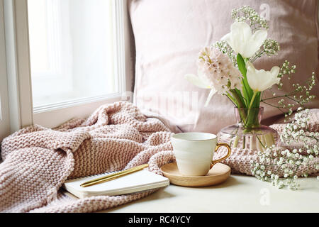 Gemütliches Ostern, Frühling noch leben Szene. Tasse Kaffee, geöffnet Notebook, pink aus Gewirken plaid auf der Fensterbank. Vintage feminin Foto. Florale Komposition mit Tulpen, Hyazinthen und Gypsophila Blumen. Stockfoto