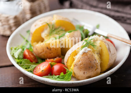 Gebackene gefüllte Kartoffeln mit Käse, Sauerrahm und Dill auf einem Teller. Gesund leckeres Abendessen Stockfoto