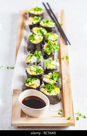 Vegane grüne Sushi Rollen mit Avocado, Sprossen, Gurke und Nori auf einem Holzbrett, grauen Hintergrund. Stockfoto